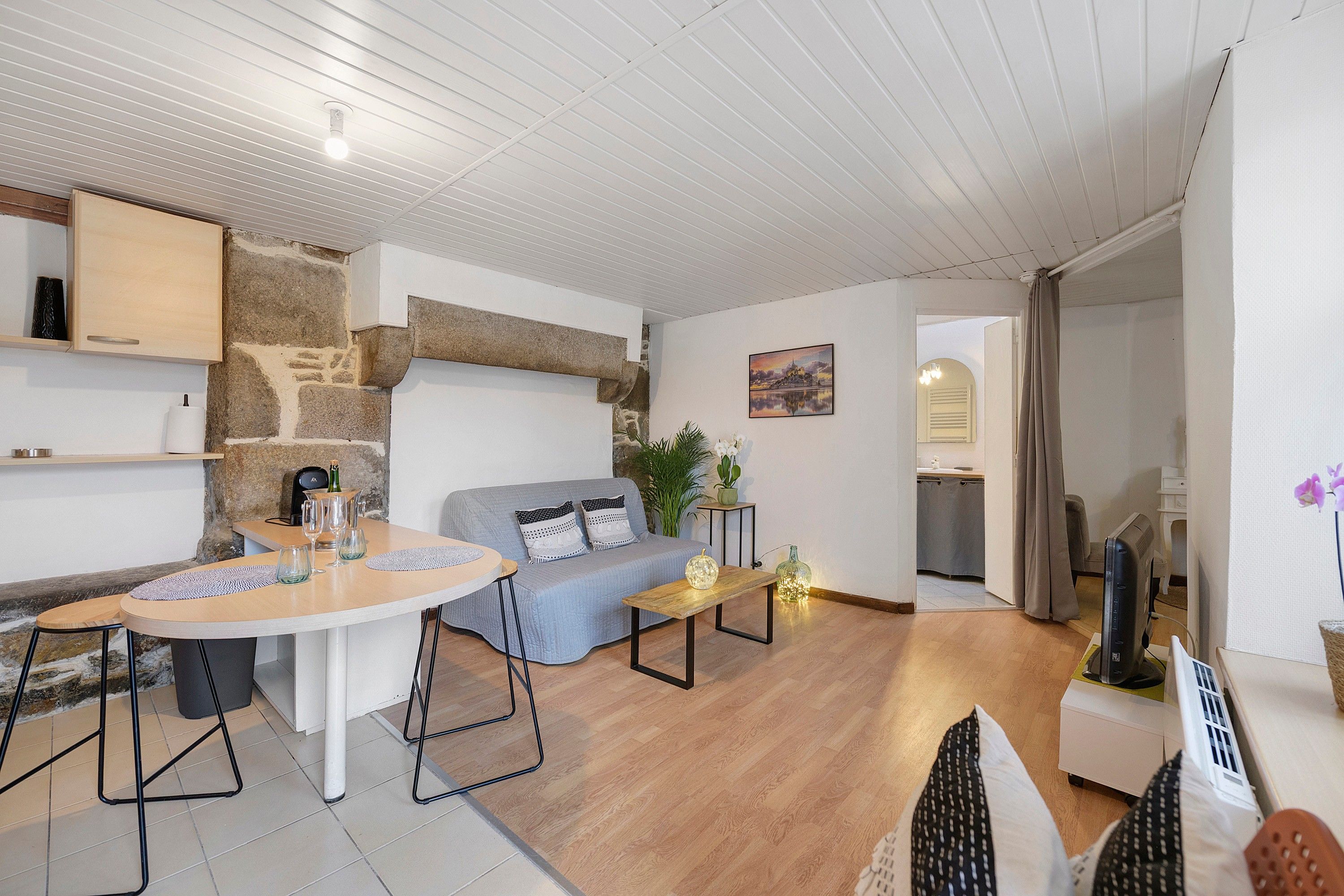 Een moderne woonkamer met een stenen muur, een bank, een salontafel en een eethoek met stoelen.