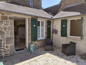 A stone building with a tiled roof, a small patio with two wicker chairs, and a door leading to an interior space. - Guesthouse 'Le 101' with private garden (Villedieu-les-Poêles-Rouffigny)