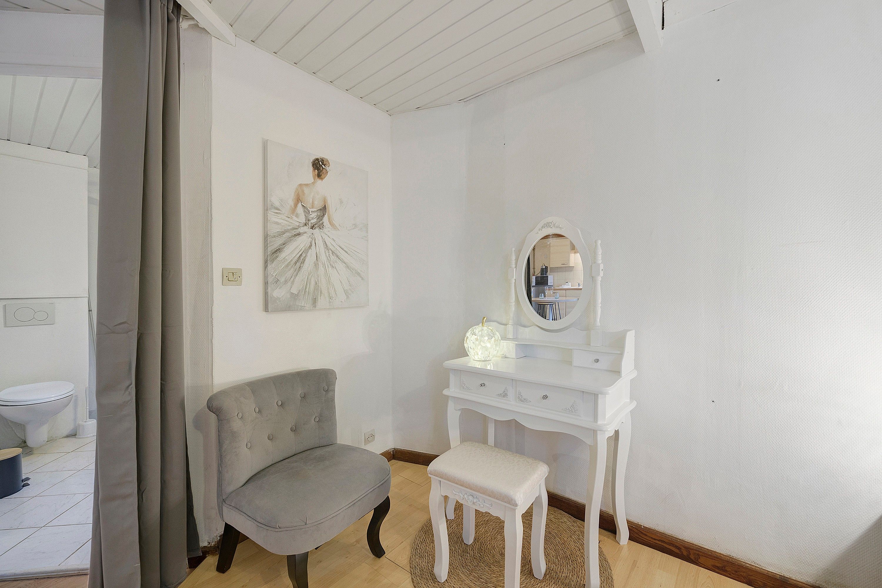 Een kamer met een witte wastafel, een grijze fauteuil, een klein wit bankje en een schilderij aan de muur.