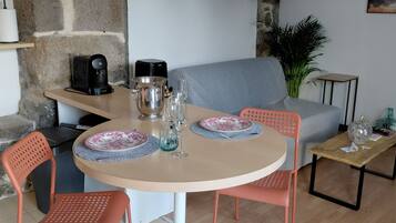 Un coin repas comprenant une table ronde, deux chaises, une machine à café et une plante.