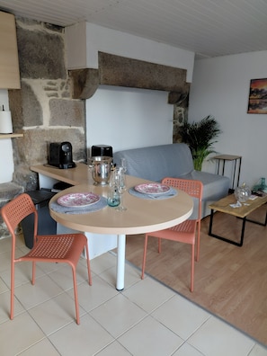A dining area with a round table, two chairs, a coffee machine, and a plant. - Guesthouse 'Le 101' with private garden (Villedieu-les-Poêles-Rouffigny)