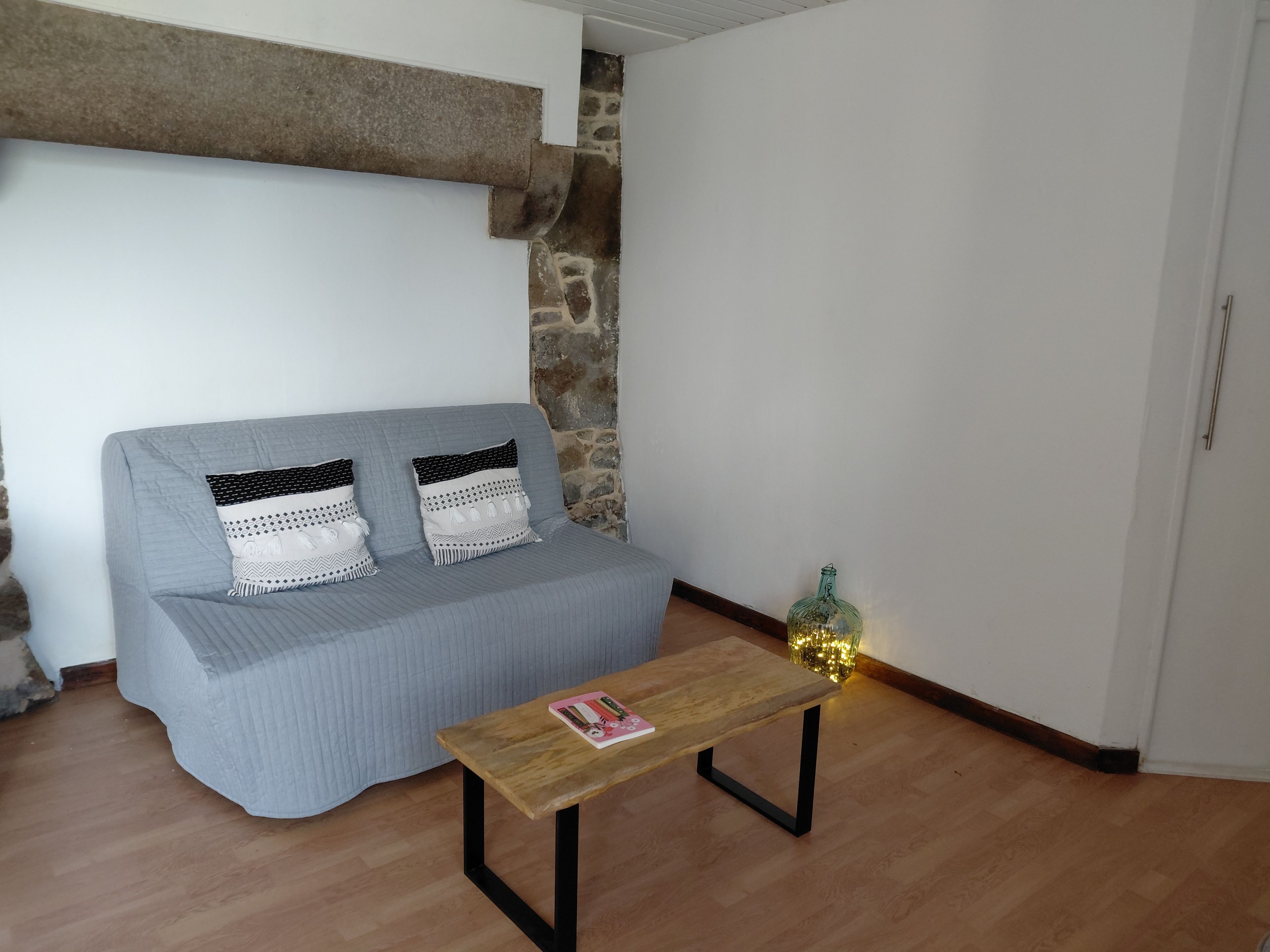 Una stanza con un divano grigio, un tavolino in legno con una rivista e una bottiglia decorativa.