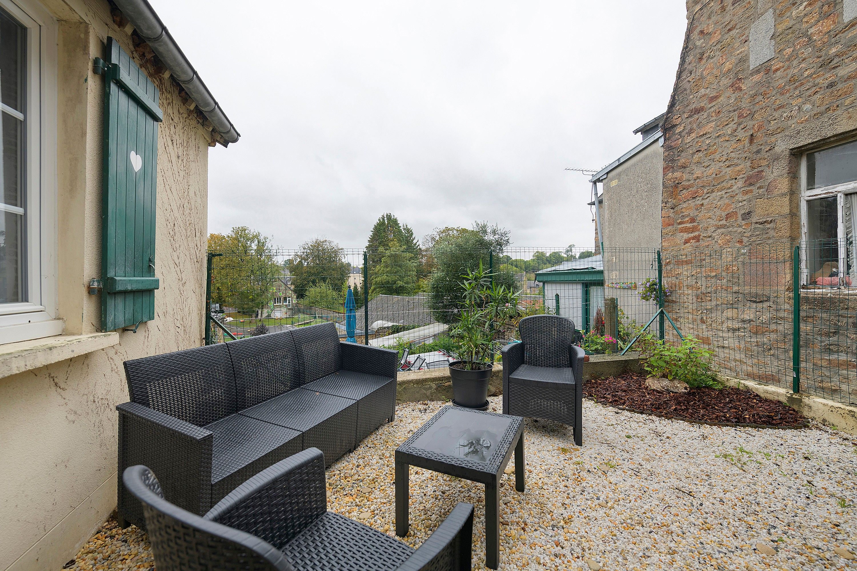 An outdoor seating area with wicker furniture, a gravel ground, and a brick building in the background.