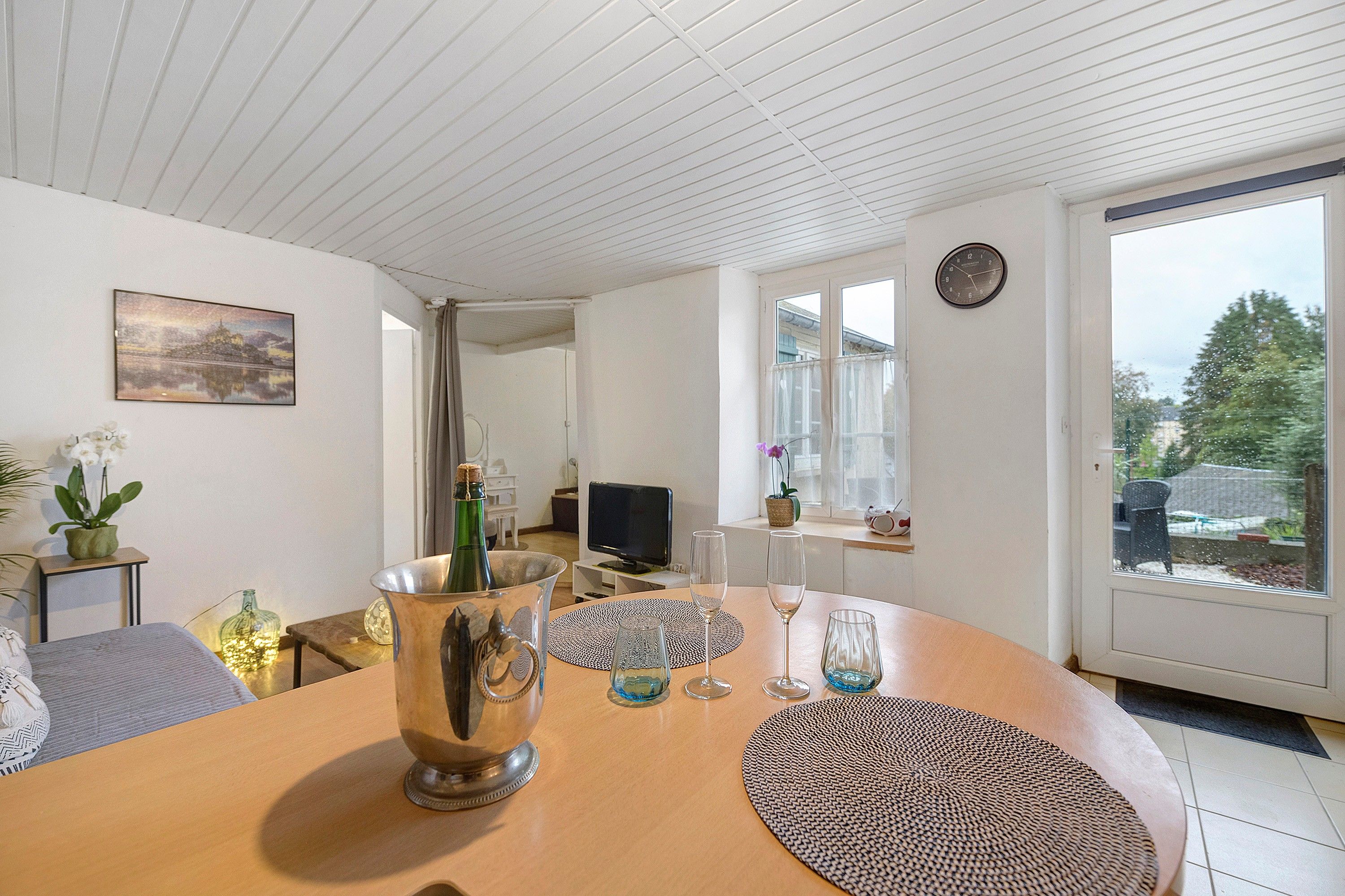 Une pièce avec une table en bois, un téléviseur et une fenêtre donnant sur un paysage verdoyant.