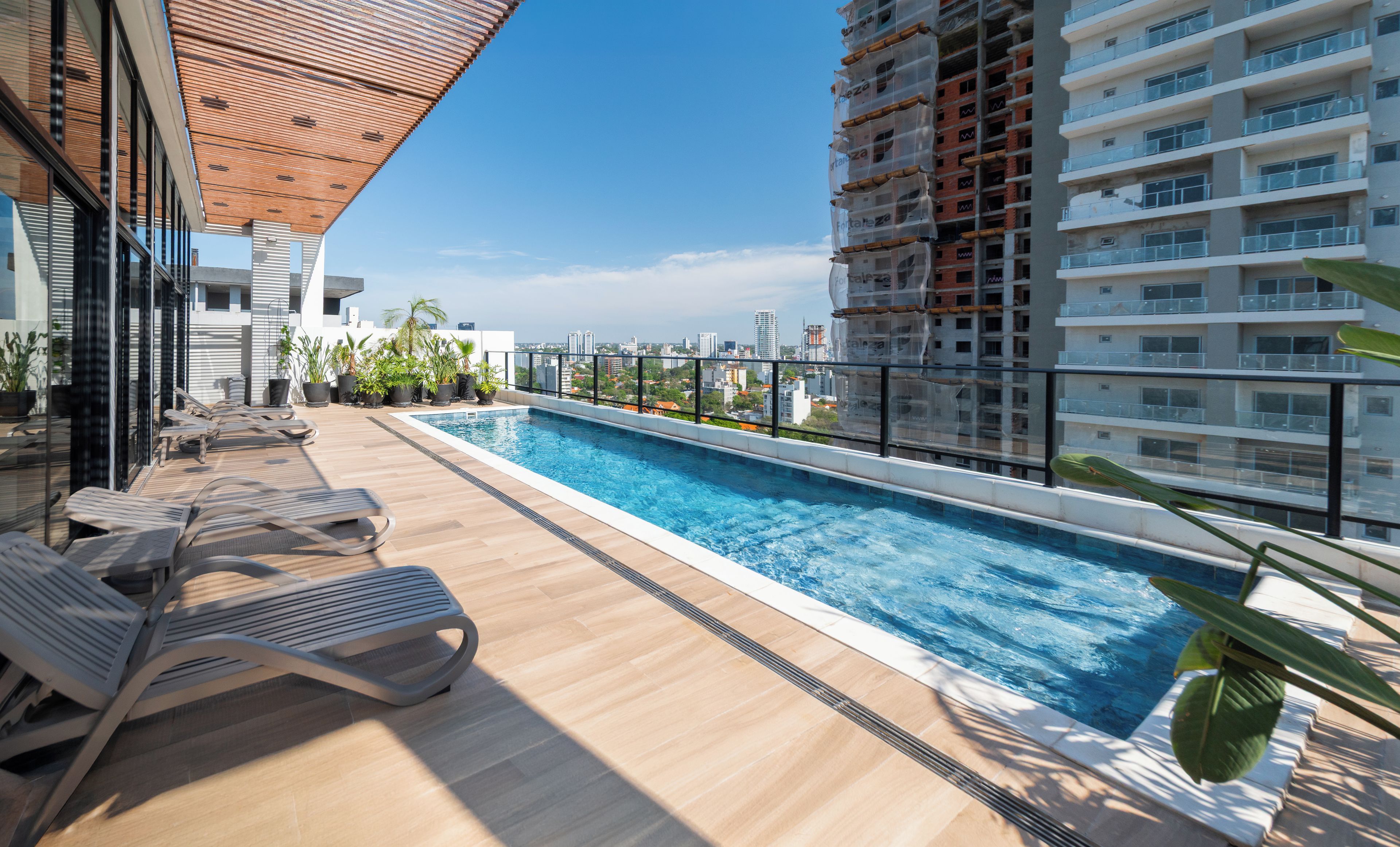 Un área de piscina en la azotea con sillones de descanso y plantas en macetas.
