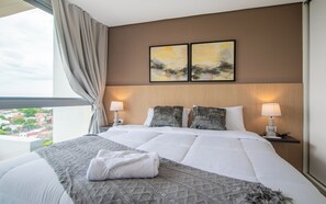 A hotel room with a large bed, two bedside lamps, a view of the city, and two paintings on the wall. - Corporate Stays Habitalis Mburucuya- 15E (Asunción)