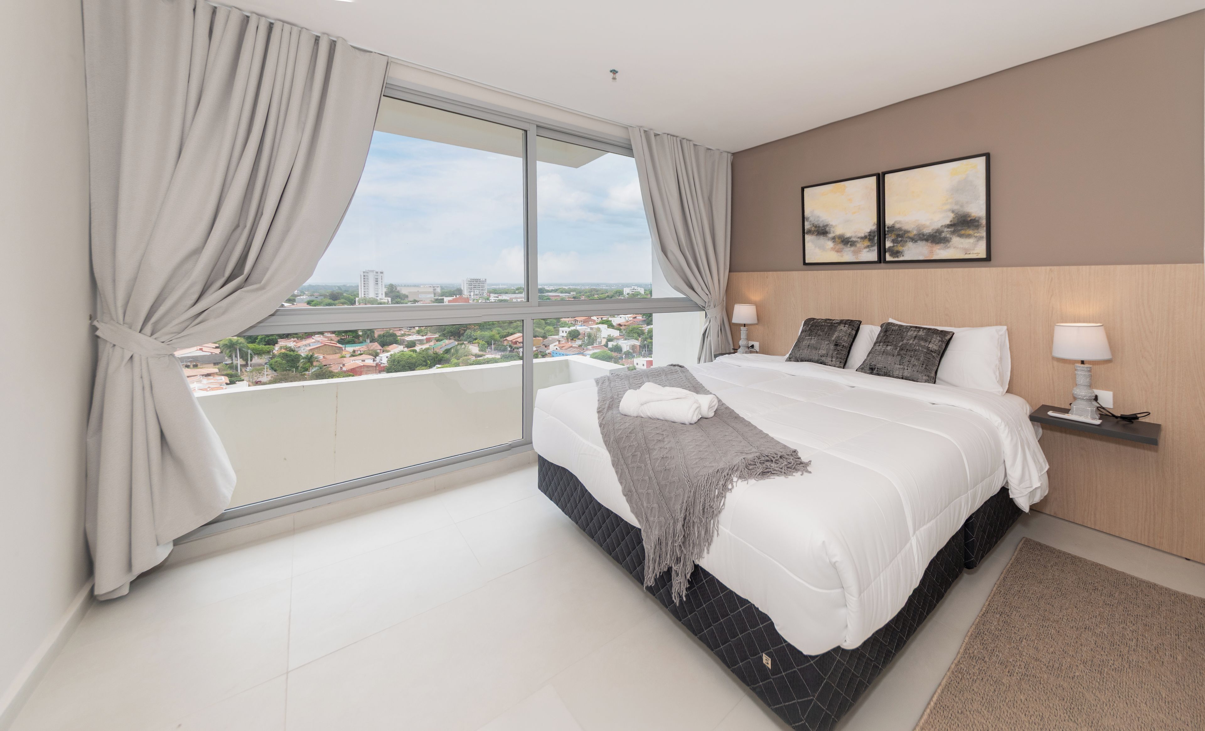 Un dormitorio moderno con una cama grande, vistas de la ciudad y una mesita de noche con lámpara.