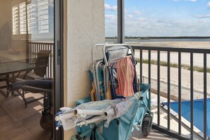 A balcony with a pool view, a beach chair, and a beach umbrella. - Carlos Pointe #224 | Beautiful Beachfront Condo, Gulf Views + Pool 🌊 (Fort Myers Beach)