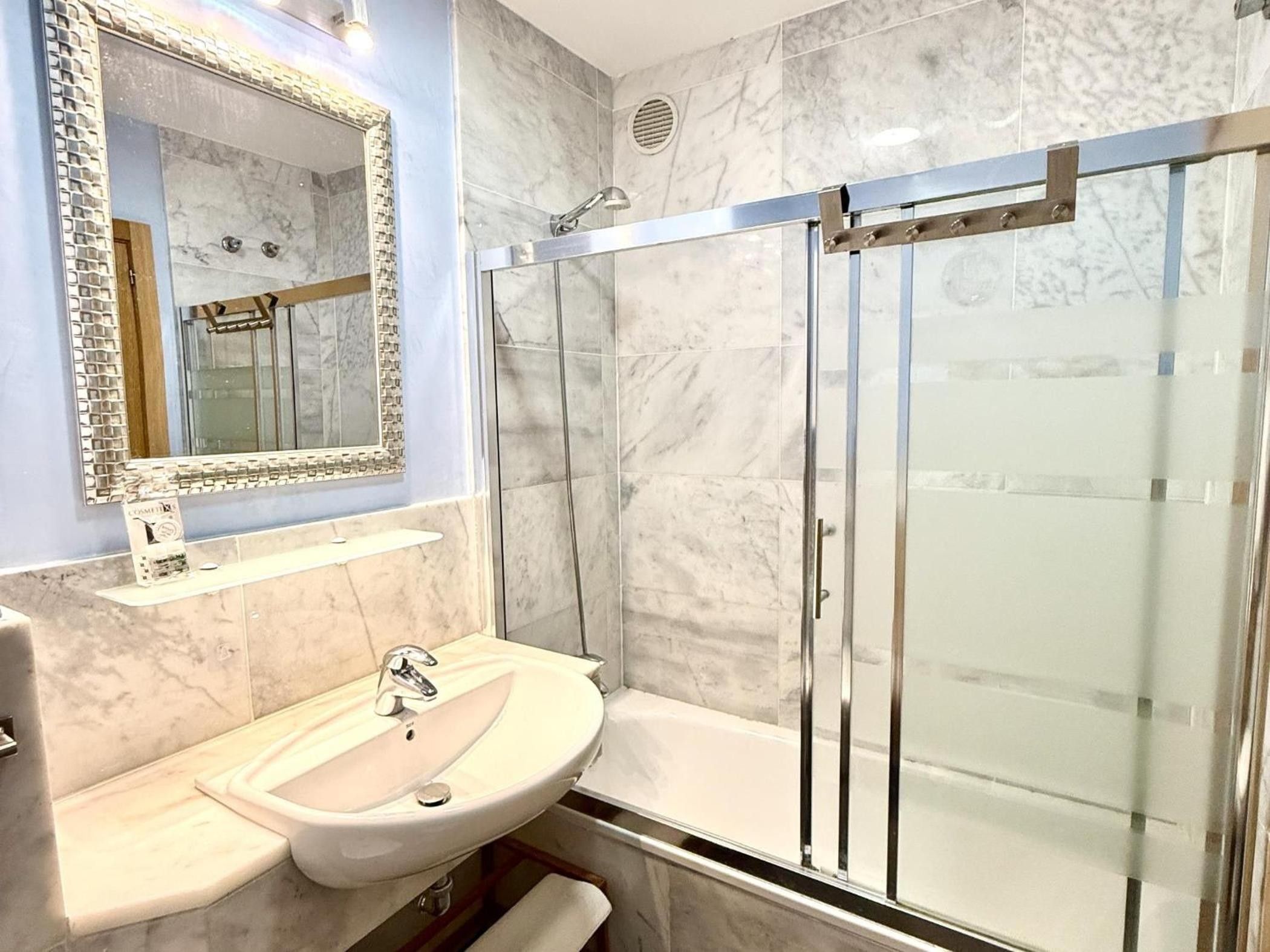 Un baño con lavamanos de mármol, cabina de ducha con mampara de vidrio y espejo con marco decorativo.