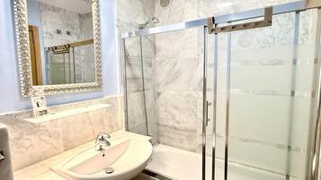 Un baño con lavamanos de mármol, cabina de ducha con mampara de vidrio y espejo con marco decorativo.