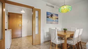 A dining area with a wooden table and chairs, a painting of a beach scene, and a ceiling light fixture.