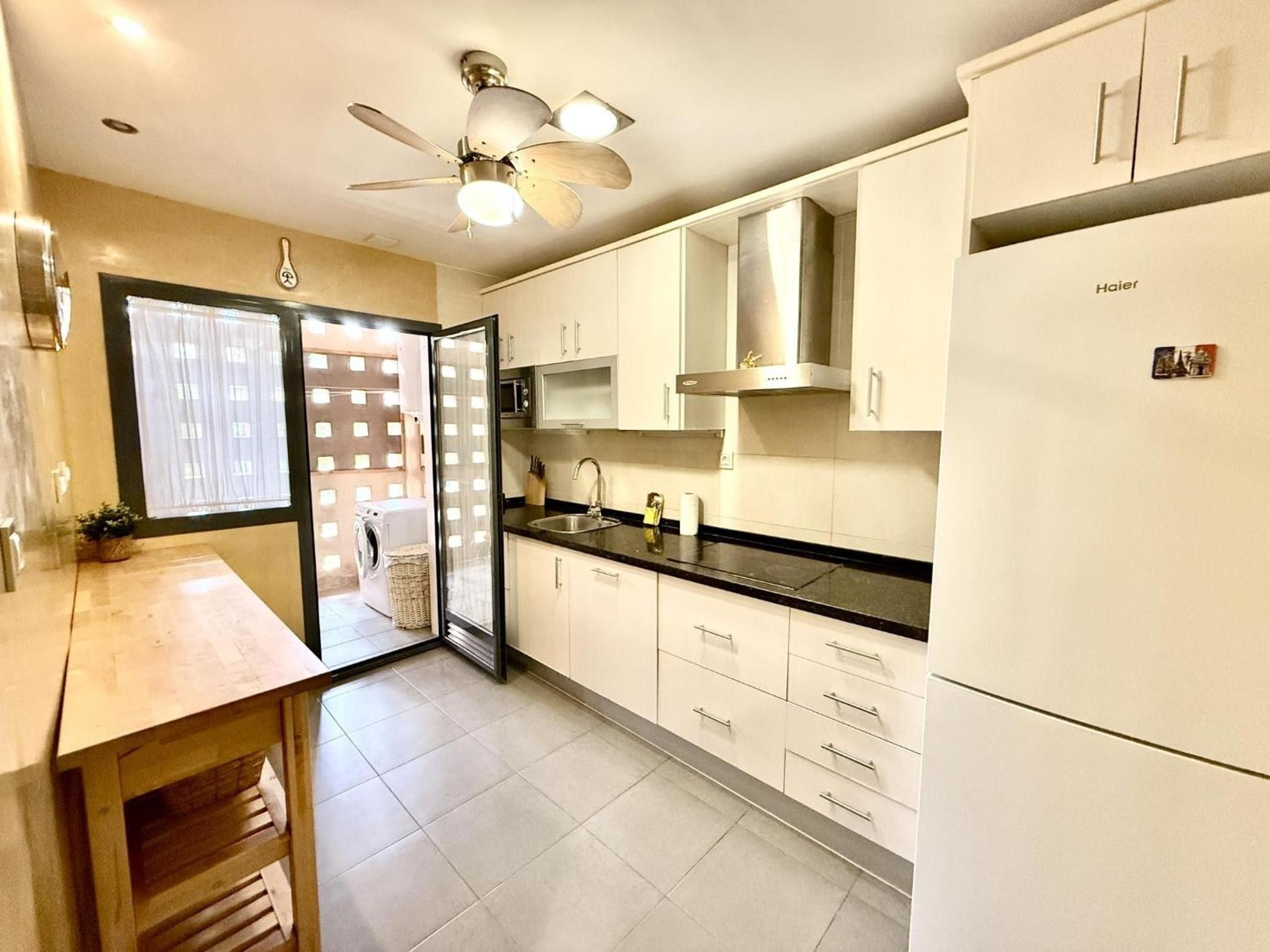 A modern kitchen with white cabinets, a black countertop, and a ceiling fan.