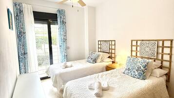 Habitación de hotel con dos camas, ventilador de techo y ventana con cortinas.