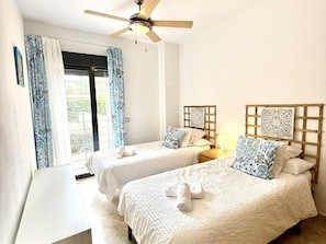 Habitación de hotel con dos camas, ventilador de techo y ventana con cortinas.