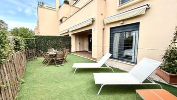 Un patio trasero con césped artificial, una mesa de madera, dos sillones de descanso y una valla de madera.