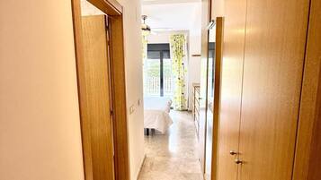 Un pasillo con puertas de madera, una cama con cubrecama blanco y una ventana con cortinas florales.
