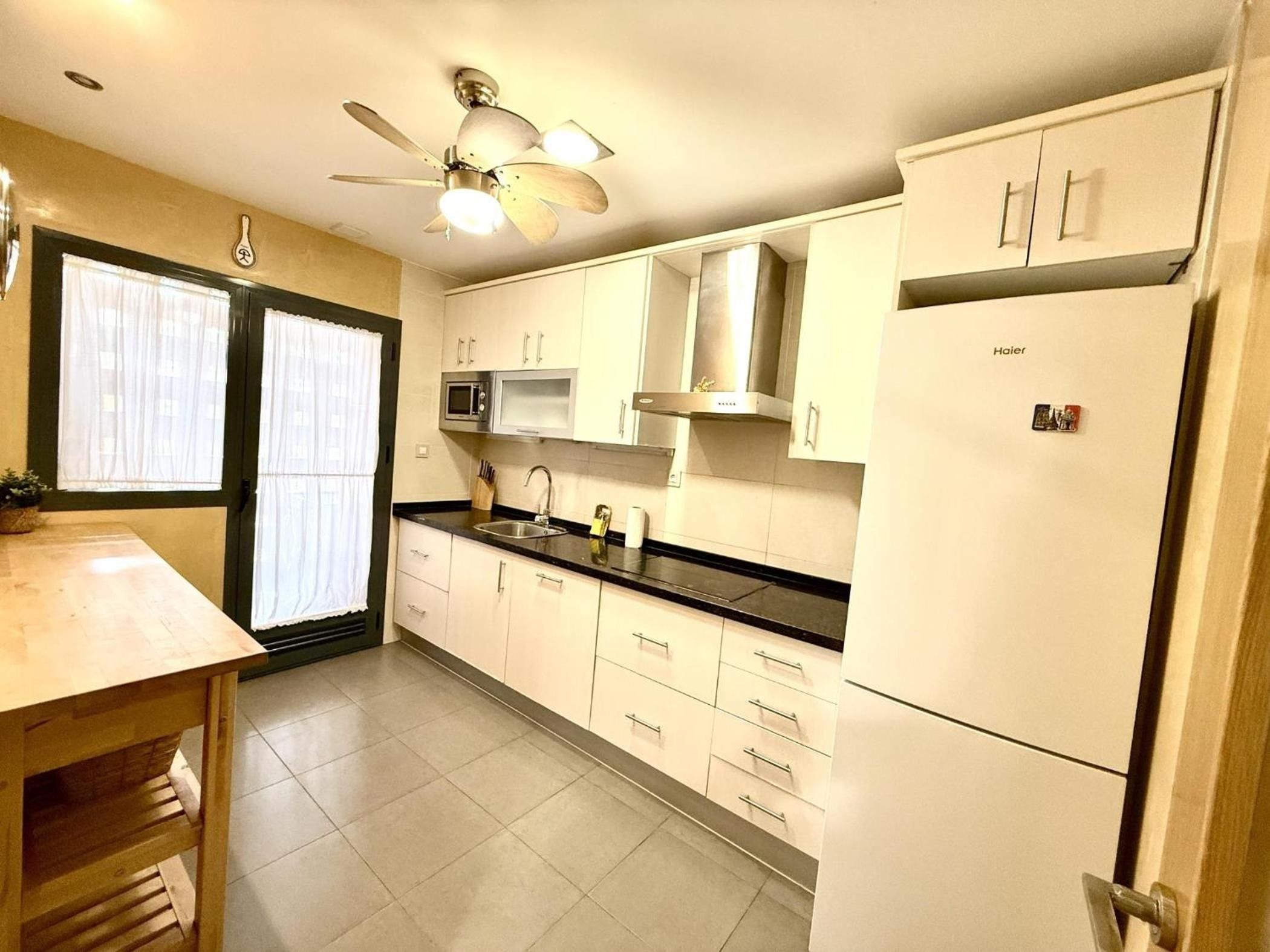 A kitchen with white cabinets, a black countertop, a microwave, a ceiling fan, and a refrigerator.
