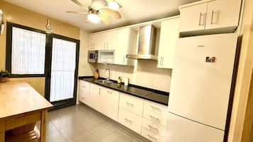 A kitchen with white cabinets, a black countertop, a microwave, a ceiling fan, and a refrigerator.