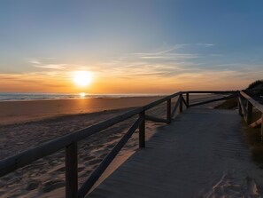 Una pasarela de madera que conduce a una playa con un atardecer al fondo.