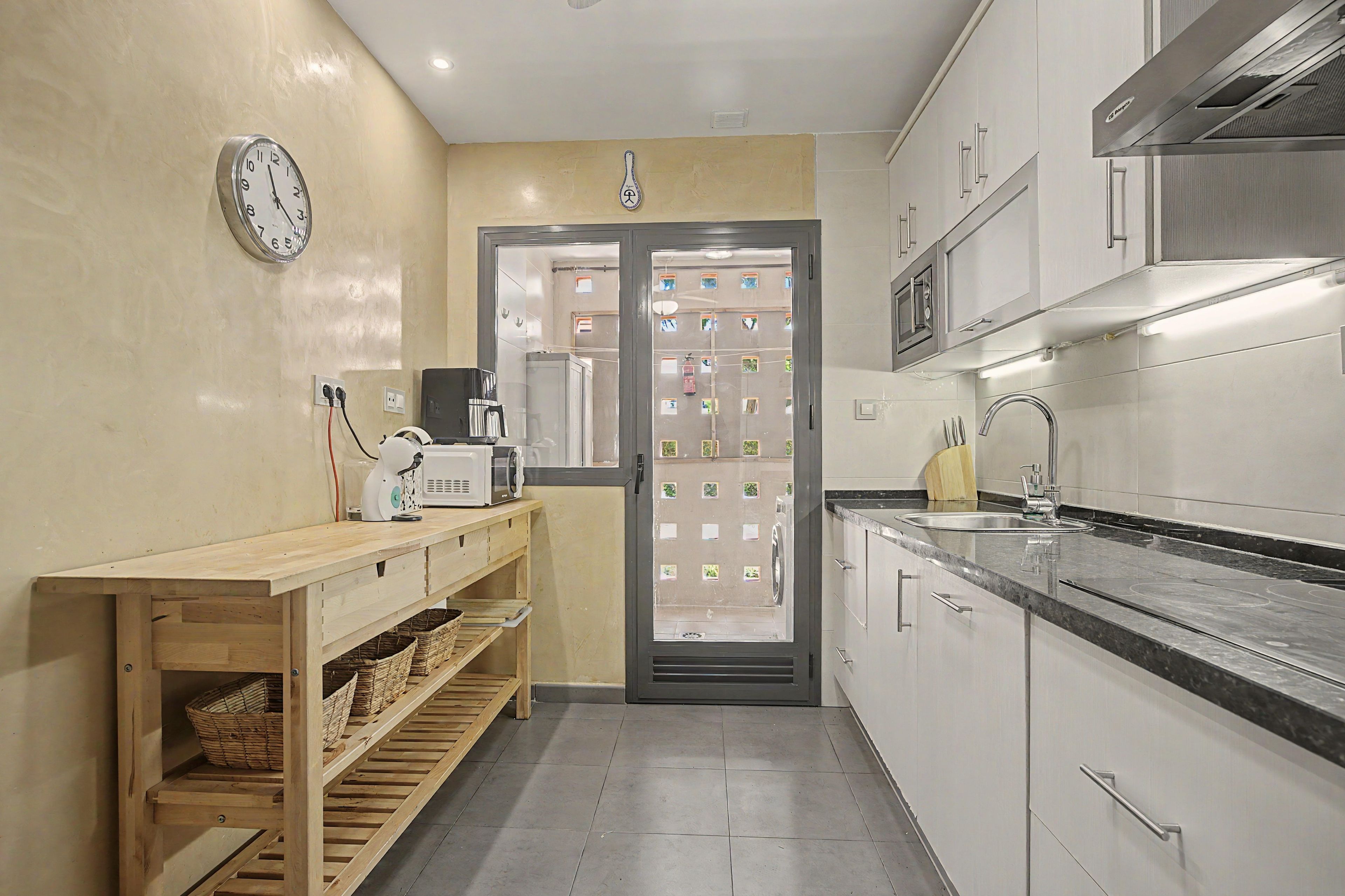 A compact kitchen with a built-in microwave, a sink, and a wooden shelf with baskets.