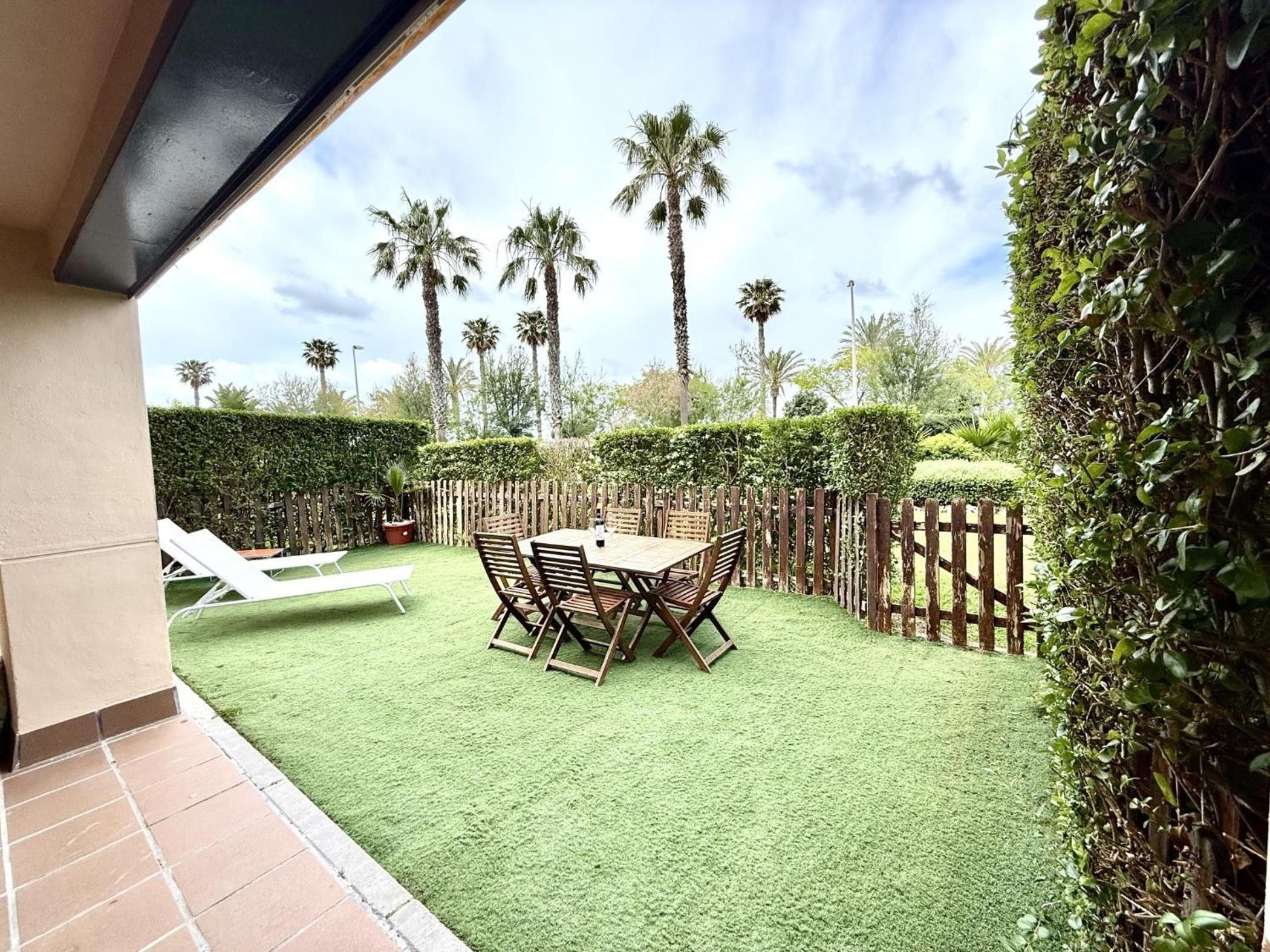 A patio with a table and chairs, surrounded by a wooden fence and palm trees.