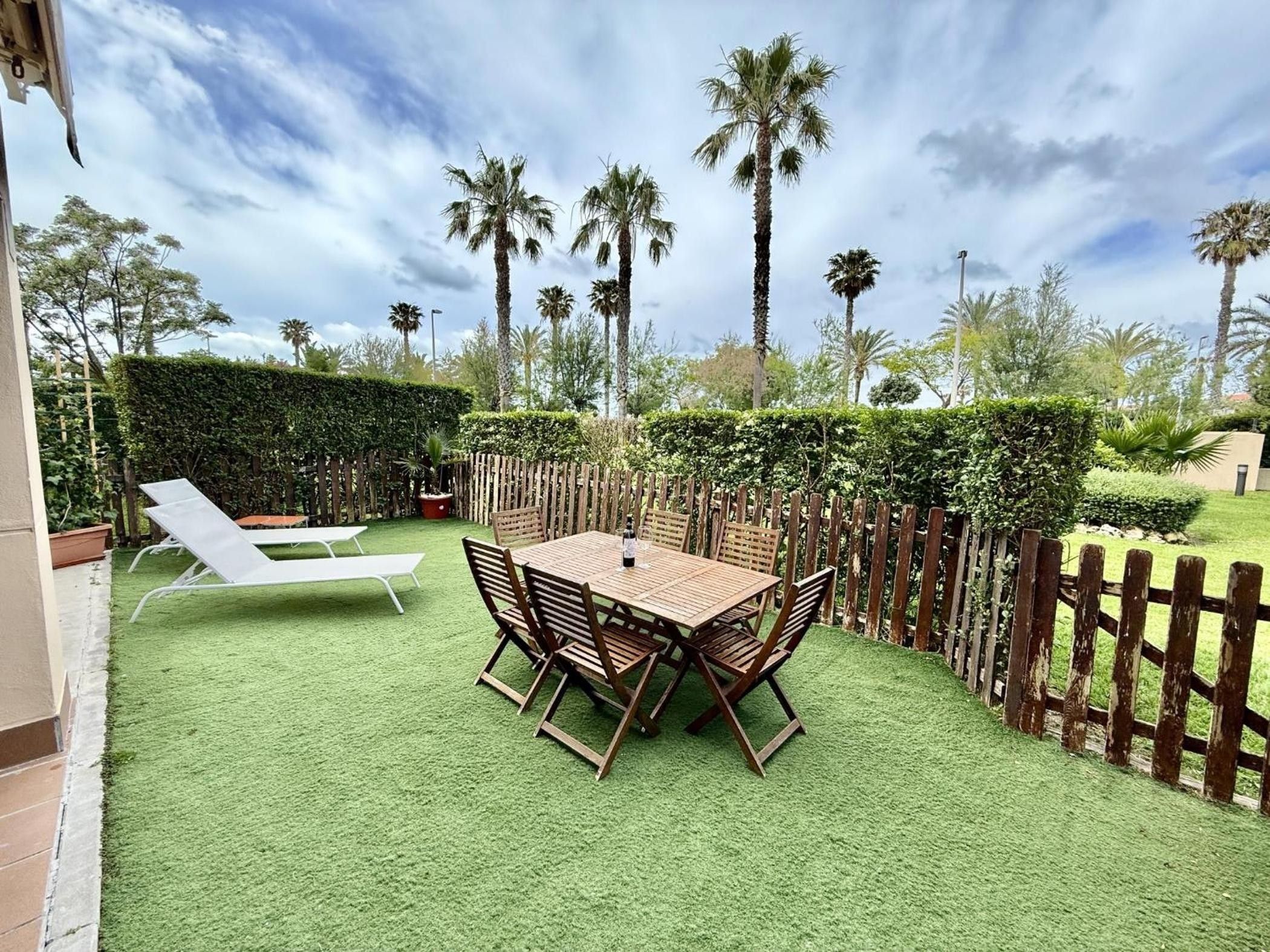 Une terrasse avec une table et des chaises, entourée d’une clôture en bois et de verdure.