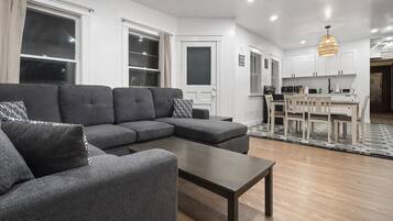 A modern living room with a sectional sofa, a coffee table, and a dining area with chairs and a table.