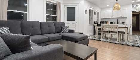 A modern living room with a sectional sofa, a coffee table, and a dining area with chairs and a table.