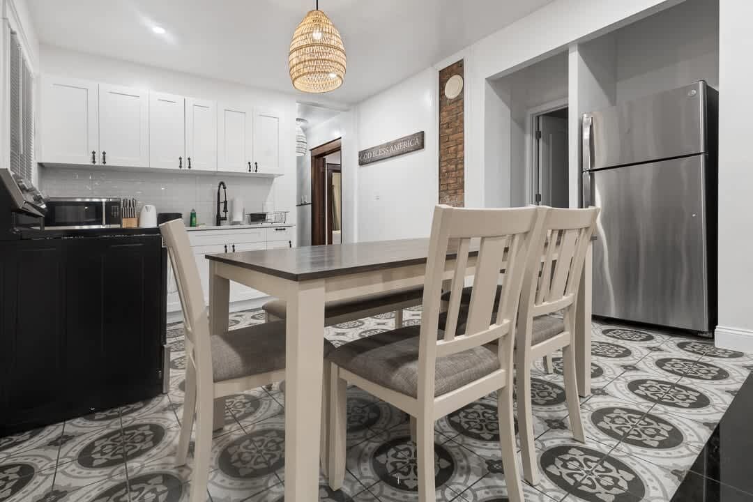 A modern kitchen with white cabinets, a stainless steel refrigerator, and a dining area with a table and chairs.