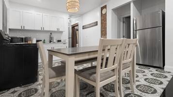 A modern kitchen with white cabinets, a stainless steel refrigerator, and a dining area with a table and chairs.