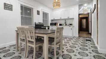 A modern kitchen with white cabinets, a dining table with chairs, and patterned floor tiles.