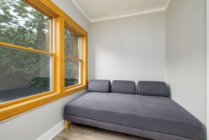 Une pièce d’angle avec une fenêtre, un canapé gris et un plancher en bois.