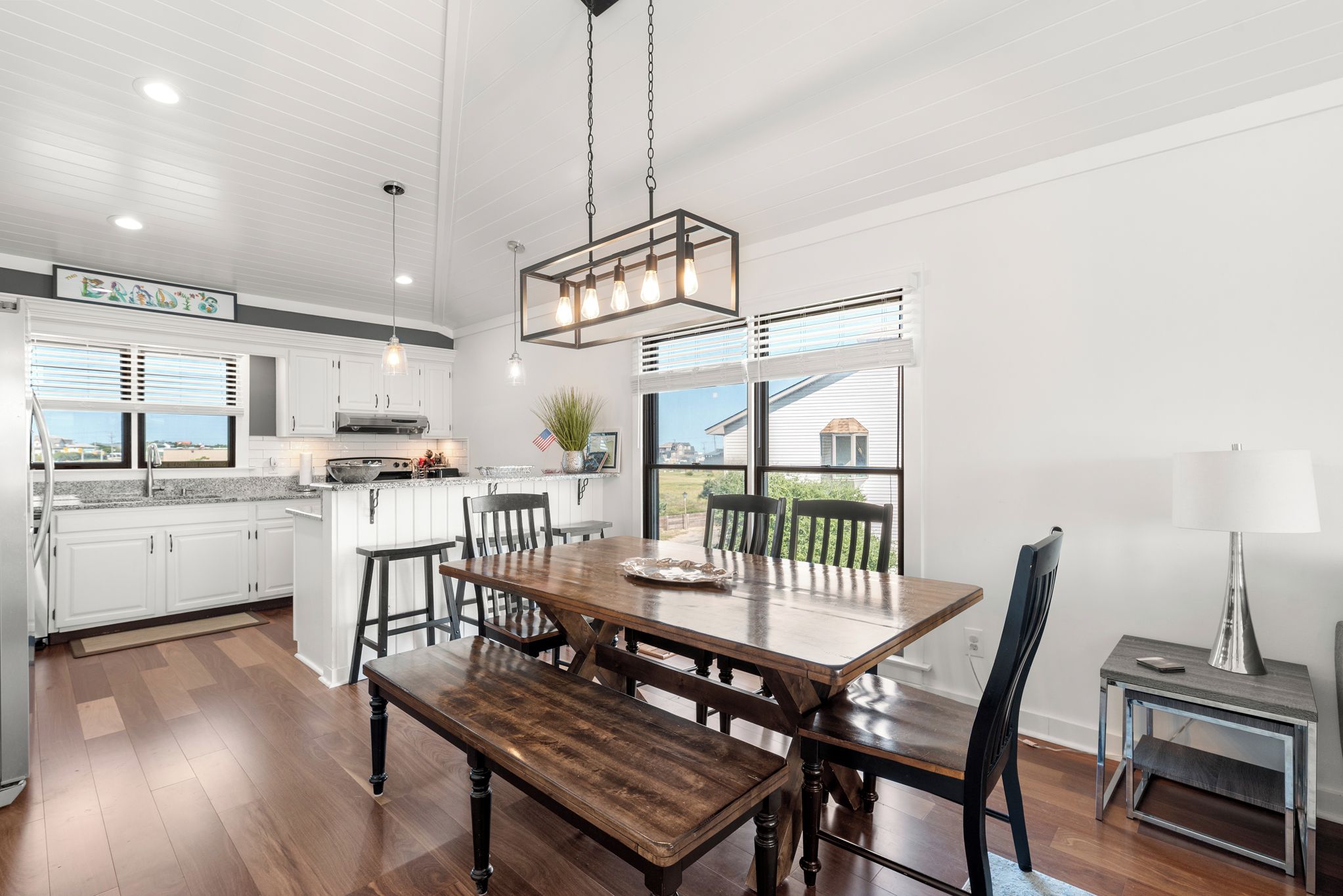 A modern kitchen with white cabinets, a wooden dining table, and a large window.
