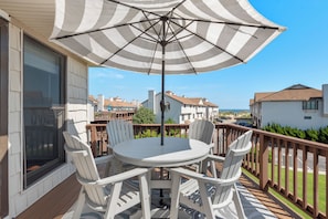 A deck with a round table and chairs, an umbrella, and a view of the neighborhood. - Sea Dunes D1: Coastal Retreat with Ocean Views (Kitty Hawk)