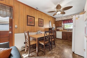 A kitchen with wooden paneling, a dining table with chairs, a ceiling fan, and a refrigerator. - Sea Bird: Live Oak Tree Swing (Kill Devil Hills)