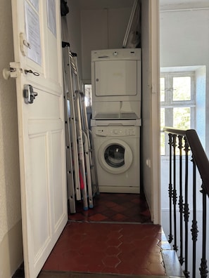 Een wasserette met een wasmachine, een droger en een trap die naar een balkon leidt.
