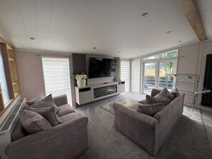 A modern living room with a flat-screen TV, grey sofas, and a large window. - Ty Mawr Holiday Park Swift Toronto Lodge (Abergele)