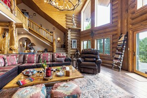 A log cabin interior with a large wooden staircase, a leather sofa, a recliner, and a dining table with a fruit platter. - Sundance Lodge in Angel Fire (Angel Fire)