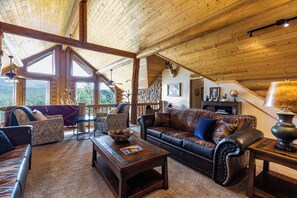 A spacious living room with a high ceiling, a leather sofa, a coffee table, and a stone accent wall. - Sundance Lodge in Angel Fire (Angel Fire)