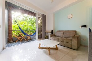 A living room with a sofa, a coffee table, a hammock, and a sliding glass door leading to a balcony with greenery. - Utopía 2.West-StylishApt•OpticalFiber•Self CheckIn (Medellín)