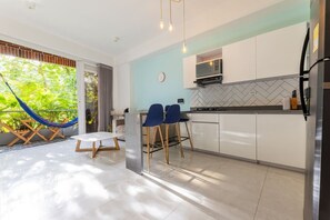 A modern kitchen with white cabinets, a microwave, and a refrigerator. There is a dining area with a table and chairs, and a hammock outside. - Utopía 2.West-StylishApt•OpticalFiber•Self CheckIn (Medellín)