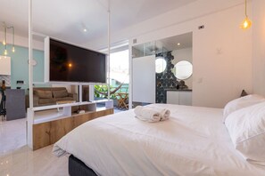 Ein modernes Hotelzimmer mit einem großen Bett, einem Flachbildfernseher, einer Sitzecke inklusive Sofa und Couchtisch sowie Blick ins Freie.