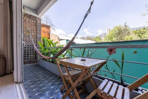 Ein Balkon mit einer Hängematte, einem Holztisch und Blick auf eine Stadtlandschaft.