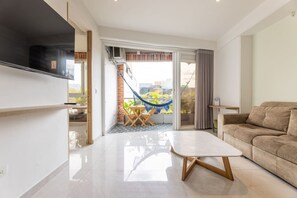 A modern living room with a flat-screen TV, a sofa, a coffee table, and a hammock outside a sliding glass door. - Utopía 4.West - Shining 2BR•Wi-Fi•AC•Self Check-In (Medellín)