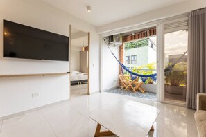 A modern living room with a flat-screen TV, a dining area with a hammock, and a sliding glass door leading to a balcony with plants. - Utopía 4.West - Shining 2BR•Wi-Fi•AC•Self Check-In (Medellín)