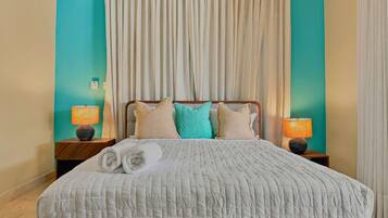 A neatly made bed with a white quilt, two bedside lamps, and a set of towels.