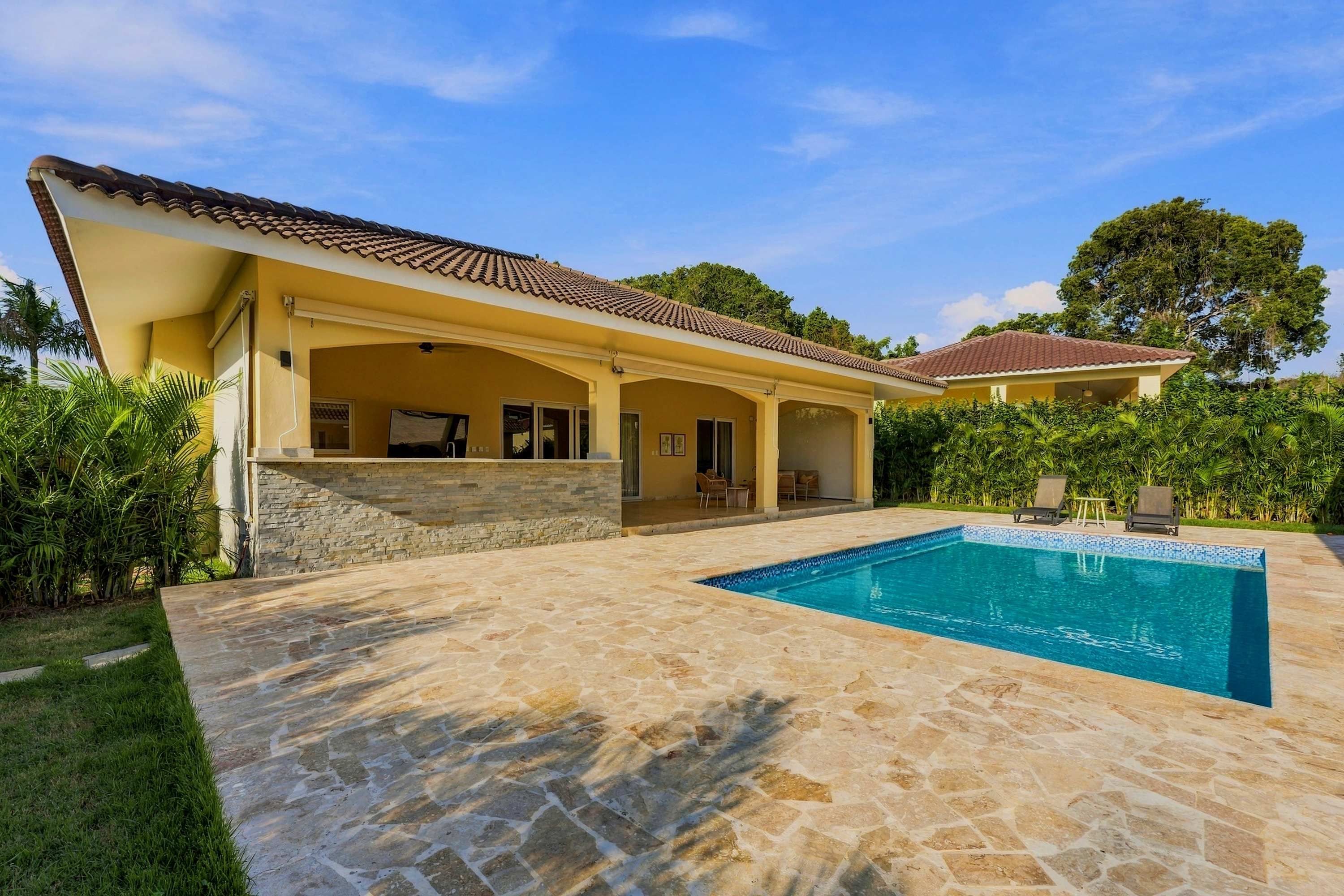 A house with a swimming pool, stone patio, and a covered outdoor area.