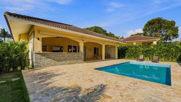 A house with a swimming pool, stone patio, and a covered outdoor area.