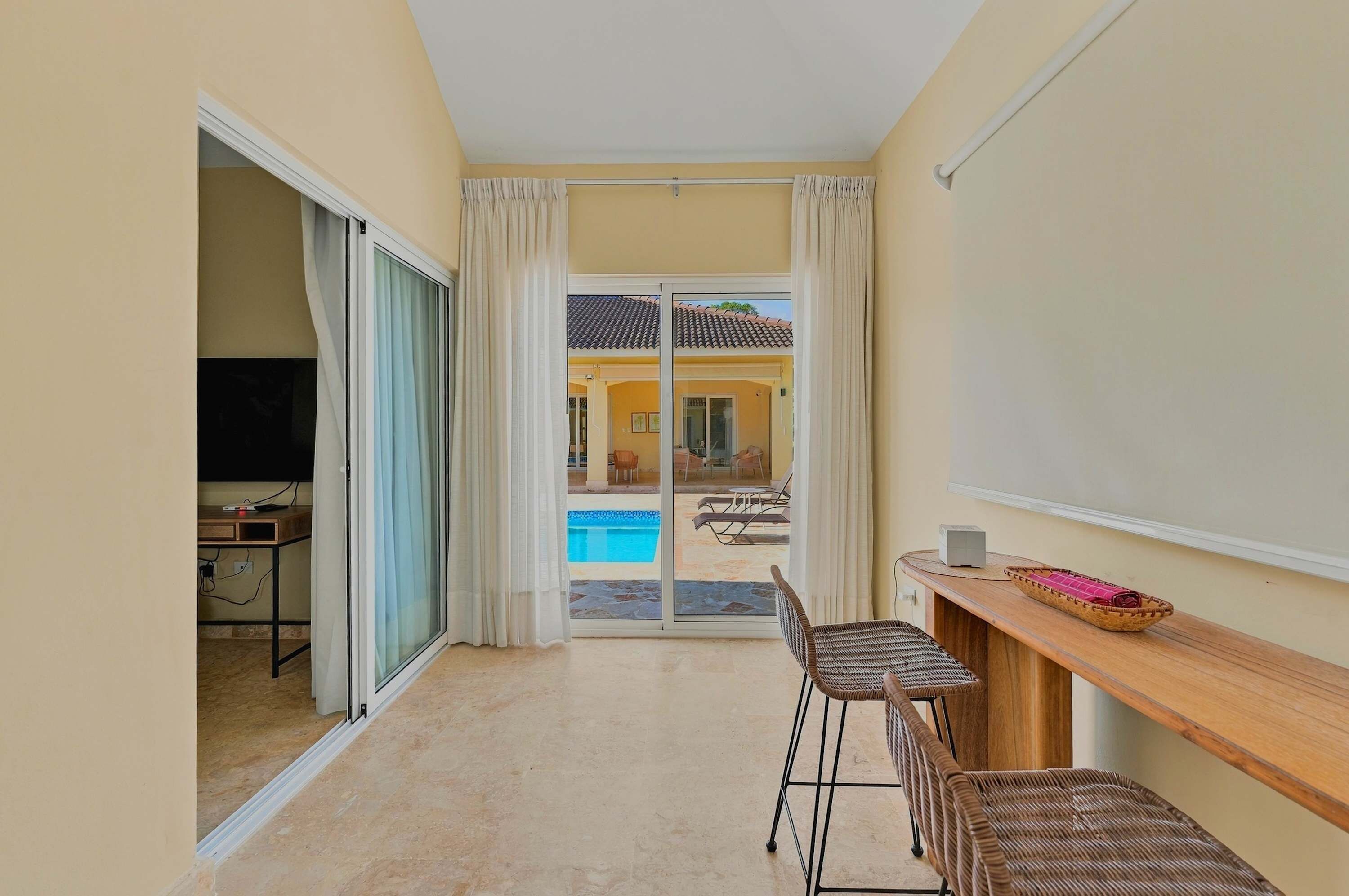 A room with a sliding glass door leading to a pool area, a wooden table with chairs, and a television in the corner.
