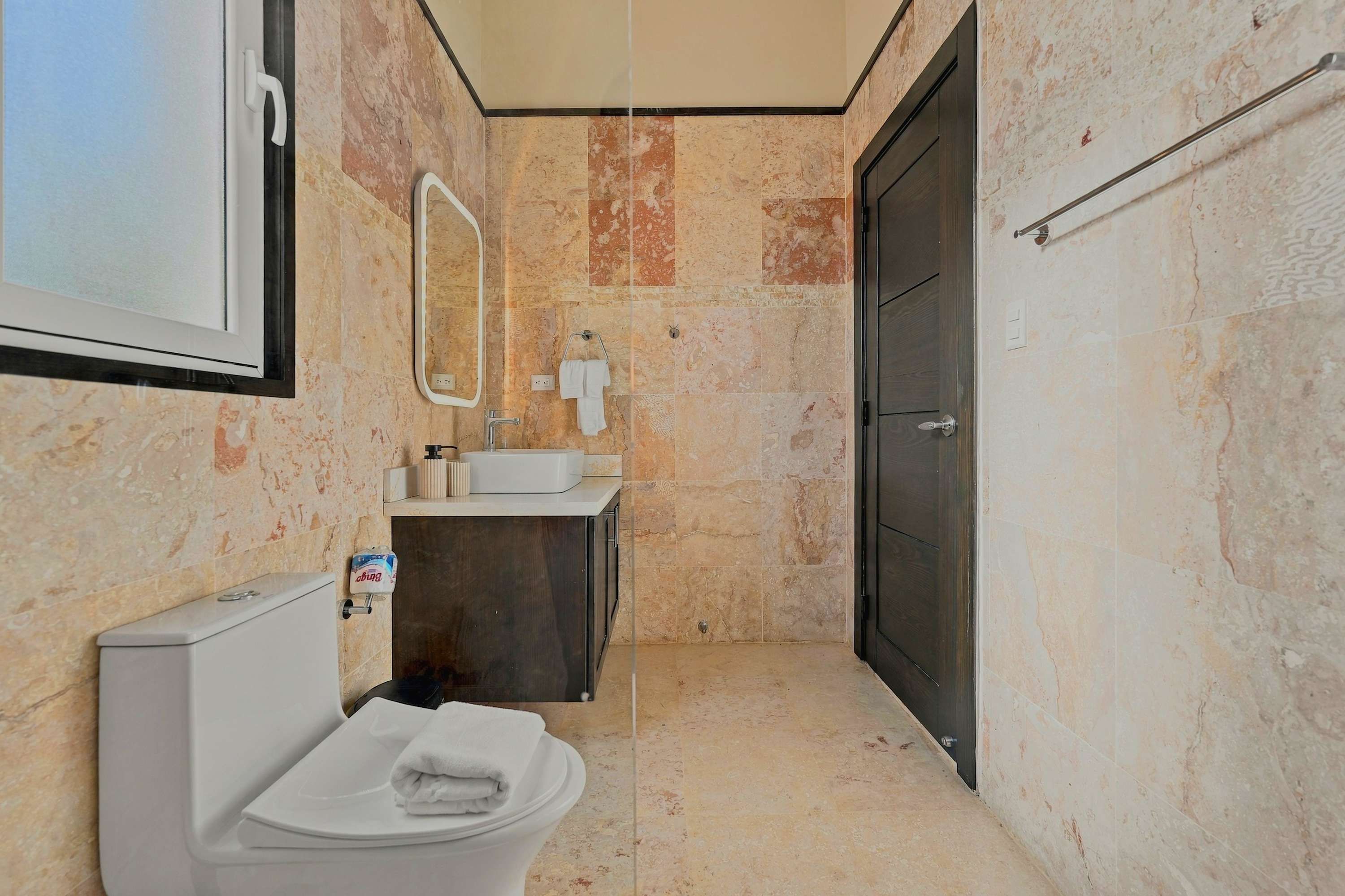 Une salle de bain avec des toilettes, un lavabo, un miroir et une porte sombre.